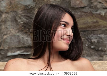 Smiling teenage european girl with dark hair and bare shoulders looking to one side.
