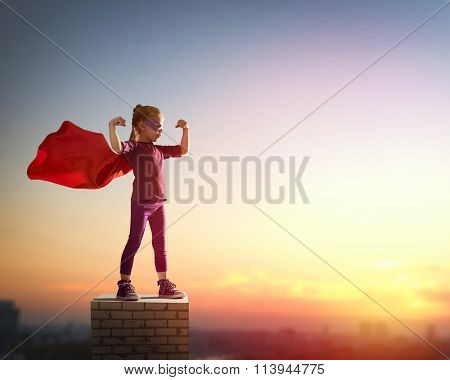 Little child girl plays superhero. Child on the background of sunset sky. Girl power concept