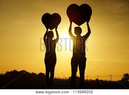 a man and a woman holding big red hearts with sunset silhouette background