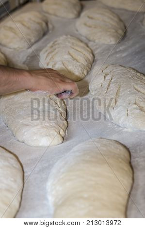 Baker Preparing And Cutting Raw Loaves To Bake In The Oven