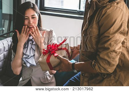 Young man is giving a present to his lovely girlfriend while they are sitting on couch at home