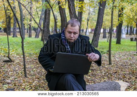 Businessman Having A Laptop In The Park In The Fall. Young Man Sitting On Tree In Park With Laptop O
