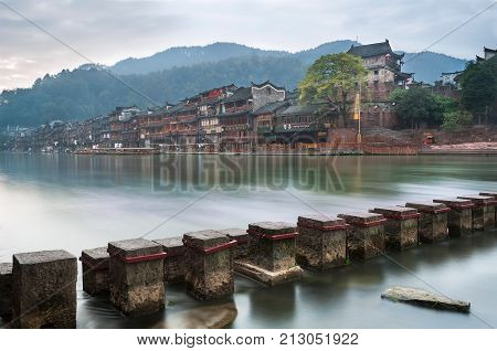 FENGHUANG, CHINA - NOV 13, 2014 - Stepping stones across the Tuojiang river with the North Gate Tower in the background in Fenghuang, Hunan Province, China.