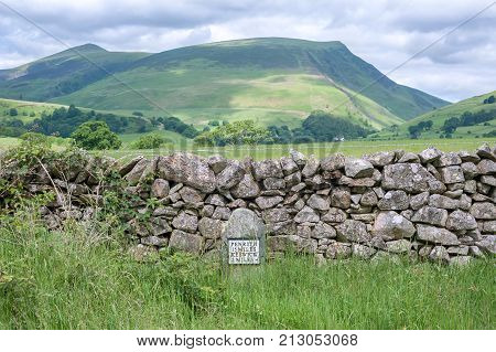 Cumbrian hills with an old-style milestone and drystone wall in the foreground Cumbria UK