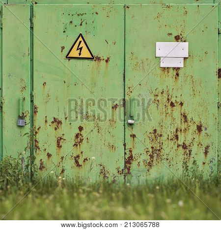 Metal rusty green door with warning high voltage sign on it.