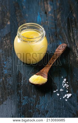 Glass of salted drawn ghee butter standing with wood spoon and sea salt over old dark blue wooden background. Healthy eating.