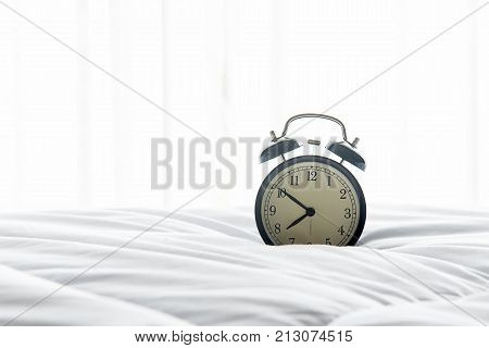 Vintage Alarm clock get up on white bed sheet duvet and pillow in morning with sunnny day. Lifestyle Concept