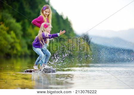 Adorable Sisters Playing By Hallstatter See Lake In Austria On Warm Summer Day. Cute Children Having