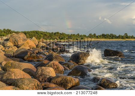 Boulders forest shore evening light sunset clouds blue sky and rainbow on the Baltic Sea. Mohni small island in Estonia Europe.