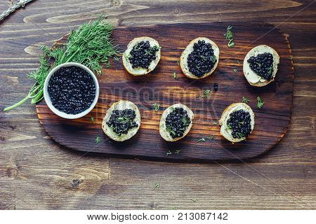 Top view of black caviar appetizers at wooden board