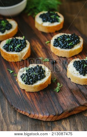 Black caviar on the pieces of bread over wooden kitchen board