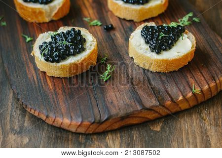Black caviar on the pieces of bread over wooden kitchen board