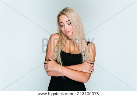 Feeling lovely. Beautiful young woman with blond hair keeping eyes closed while standing
against grey background