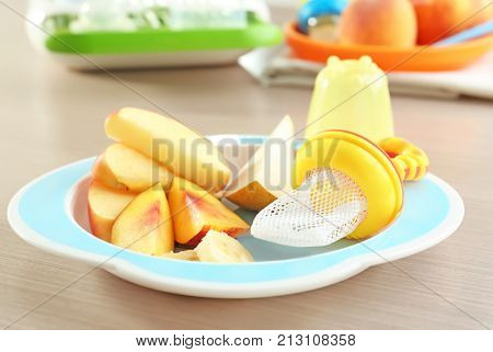 Plate with sliced fruits and baby's nibbler on table
