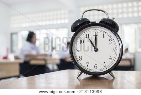 Closeup of Retro alarm clock with ten o'clock on table teacher in blur students exams classroom. Time is indefinite continued progress of existence. Education concept selective focus.