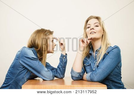 Woman saying bad things about her over confient female friend. Pointing at forehead stupidity gesture.
