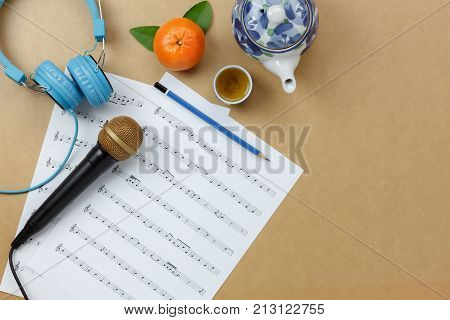 Above view shot of accessories musical instrument and Chinese new year concept.Music sheet note paper & microphone also blue headphone with teapot and orange for decor festival.Copy space design text