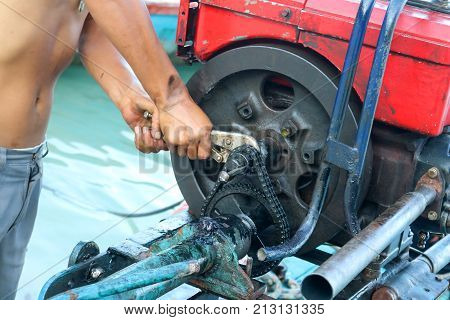 Men are repairing engines adapted for long-tail boats. Maintenance the chain gear and equipment for modified old diesel engine and spare parts in Thailand.