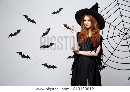 Halloween Witch Concept - Happy Halloween Witch Pointing Finger On Side Over Dark Grey Studio Backgr