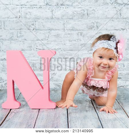 Beautiful and cute girl in pink dress with the letter N. Emotional girl