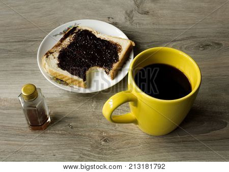 a yellow cup of coffee and saucer with bited sandwich on gray wooden table
