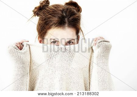 Funny cute young woman is smiling into the camera while covering her face with the collar of her sweater. Lifestyle concept.