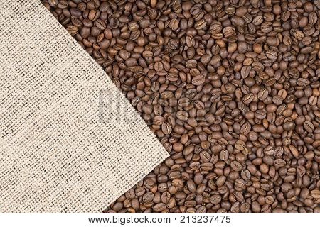 Many grains of roasted coffee as a background. Sacking on scattered coffee with space for text. Coffee beans on burlap background