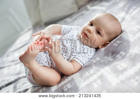 Charming boy in a white sunny bedroom. A newborn baby is resting in bed. Kindergarten for small children. Textiles and bedding for children. Family morning at home. A newborn baby with brown eyes in white panties and a T-shirt lies on the bed