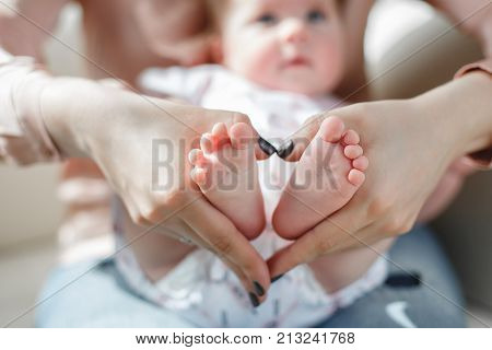 On the lap of a loving mother lies a newborn baby with fluffy little hair, mother gently supports the bare feet of the child with her hands, mother in a pink shirt and blue jeans, mother with a small son on the sofa concept of maternal love