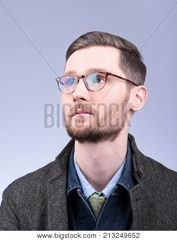 Men's style. Vertical portrait of a young man with a beard and neat hair. Denim clothing and coats. Neutral grey background