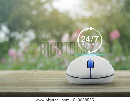 24 hours service icon with wireless computer mouse on wooden table over blur pink flower and tree Full time service concept