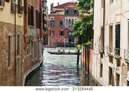 Some Tourists Enjoy A Trip In A Gondola, Along A Canal In Venice
