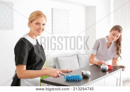 Chambermaid teaching trainee to clean table from dust