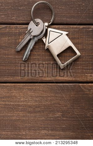 Two steel keys with house shaped trinklet on keyring on brown rustic wooden background with copy space. Home key, safety, security, real estate and rent concept, top view