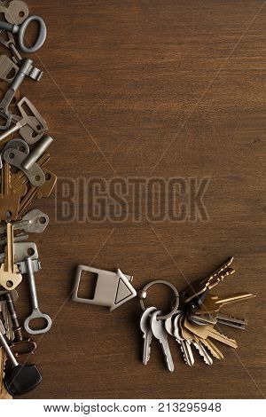 Bunch of keys with house shaped trinklet against wooden background and collection of different keys. Safety, security and real estate concept, top view, copy space