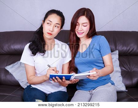Two Woman Write A Book On Sofa In Living Room At Home