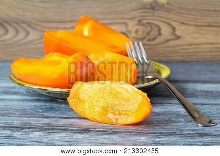 Sliced of a ripe orange persimmon on a saucer. A green saucer with fruit and a fork on a wooden table. Close up selective focus