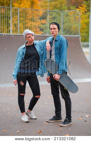 Young guy and girl skateboarders, outdoors on a bright autumn day with a skateboard in hand, the girl put her hand on the guy.