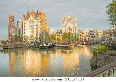 ROTTERDAM HOLLAND- AUGUST 23 2017; sun rises and catches buildings across canal and shadows old style boats moored beneath the Gothic style building known as Whitehouse
