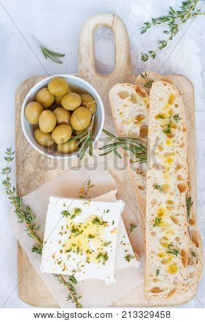 Green olives feta cheese and fresh ciabata on a wooden board light background top view.