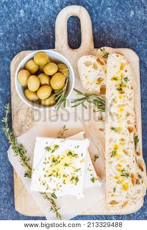 Green olives feta cheese and fresh ciabata on a wooden board dark background top view.