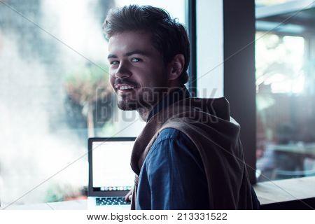 Handsome and cheerful. Portrait of handsome young man looking at camera with smile
while sitting in cafe