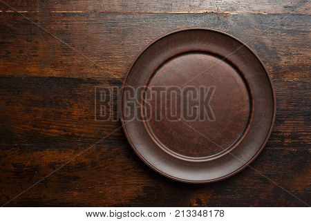 empty flat clay plate on a brown wooden background top view space for text