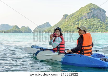 Two women are mother and daughter using a camera take pictures on kayak while travel by boat with happy on the sea during summer at Ko Wua Ta lap islands
