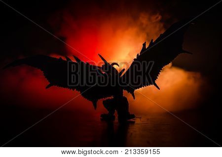 Silhouette Of Fire Breathing Dragon With Big Wings On A Dark Orange Background. Empty Space