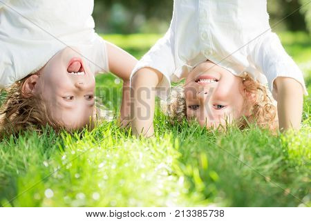 Happy children standing upside down on green grass in spring park. Healthy lifestyles concept.