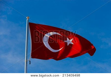 Flag of Turkey on flagpole waving in the wind against the blue sky close up
