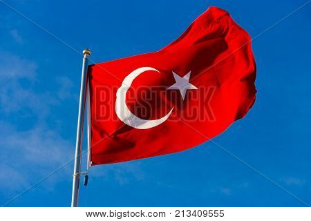 Flag of Turkey on flagpole waving in the wind against the blue sky close up