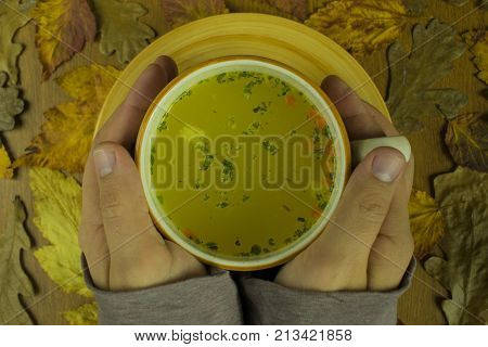 cup of hot soup warming hands autumn in yellow leaves
