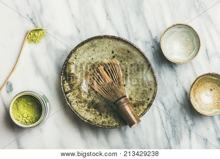 Flat-lay of Japanese tools and ceramic bowls for brewing matcha green tea. Matcha powder in tin can, Chashaku spoon, Chasen bamboo whisk, Chawan bowl, cups for ceremony, grey background, top view
